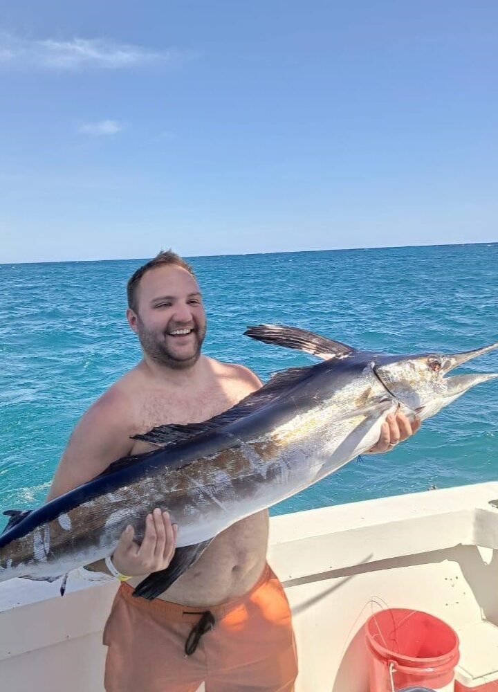 Happy tourist holding large marlin fish on taxiboat in Punta Cana waters during deep sea fishing tour